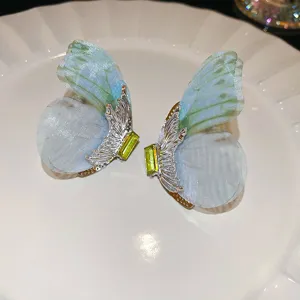 Close-up detail of fairy-style butterfly wing earrings with gradient mesh and green crystal.