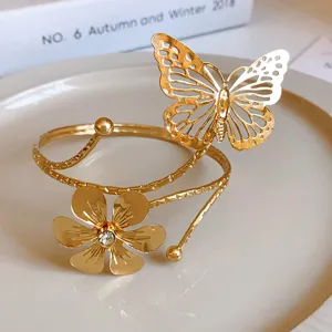 Bracciale da braccio aperto dorato con farfalla traforata e fiore scintillante di strass.