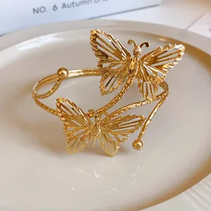 Dettaglio ravvicinato del bracciale rigido aperto in metallo dorato con farfalla traforata.