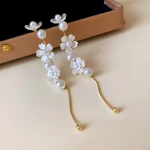 Detailed close-up of long flower pearl tassel earrings, elegant white floral design with gold.