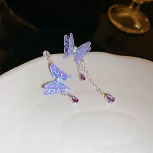 Close-up detail shot of purple gradient enamel butterfly earrings with hanging crystal chains.