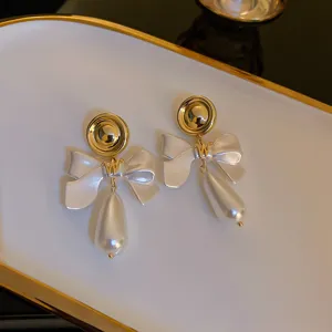 Elegant white bow and pearl drop earrings for women, stylish gold-toned metal design.
