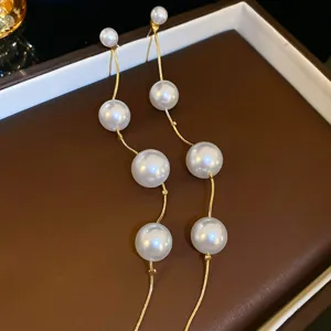Close-up detail of long tassel pearl earrings with gold chains and multiple white pearls.