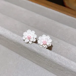 Detailed close-up of elegant white flower stud earrings with pink center on velvet tray.