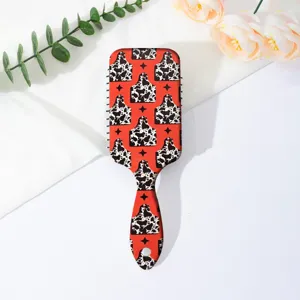 Close-up detail of the red cow print cushion hair brush, showing smooth pattern surface and handle.