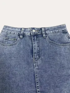 Denim skirt detail view featuring light blue acid wash finish, waist loops and metal button.