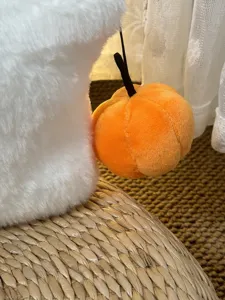 Dettaglio cuscino in peluche bianco morbido con ciondolo a zucca arancione per arredamento.