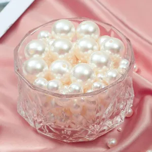 Detailed shot of white imitation pearl loose beads in a clear bowl on pink fabric for DIY crafts.