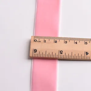 Pink velvet ribbon detail view showing width measurement with a wooden ruler for DIY crafts.