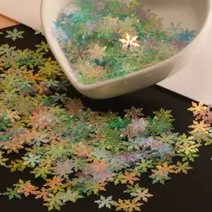 Gros plan de sequins en forme de flocon irisés sur fond sombre pour loisirs créatifs.