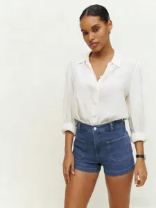 Scatto dettagliato di un'elegante camicia bianca a maniche lunghe abbinata a shorts di jeans.
