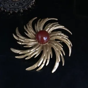 Close-up detail of a vintage gold-plated swirl brooch featuring a vibrant red center stone.