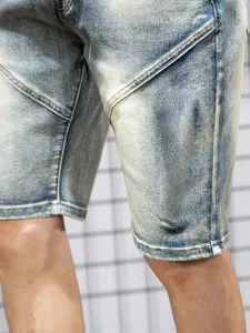 Close-up detail of mens washed denim shorts, light blue fabric texture and diagonal stitching design.