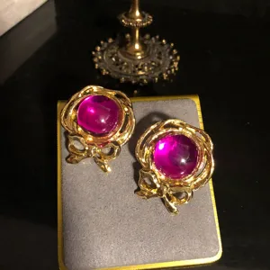 Detailaufnahme von Vintage-Ohrringen im Hofstil mit lila Glasstein und Schleifen-Design.