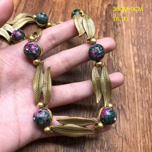 Vintage style statement necklace detail, golden leaf charms and colorful gemstone beads closeup.