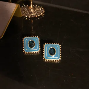 Gros plan détail de boucles d'oreilles carrées émaillées bleues avec cristal central