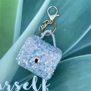 Close-up of a mini sequin tweed charm bag with a gold keychain hook on green leaves.