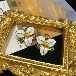 Primo piano dettagliato di orecchini floreali vintage dorati con petali in smalto bianco.