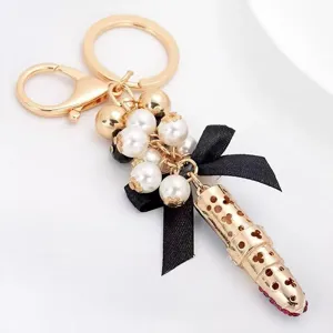 Exquisite lipstick pearl keychain detail, gold metal bag charm with elegant black bow.