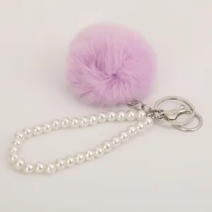Close-up detail of fluffy pom-pom and pearl bracelet keychain, cute plush bag pendant.