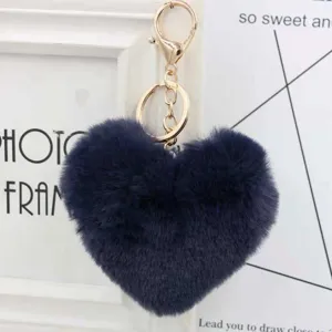 Close-up of fluffy dark blue heart plush pompom keychain with gold hardware for bag charm.