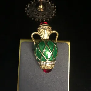Close-up view of vintage gold-tone amphora brooch with green enamel, rhinestones and red gems.