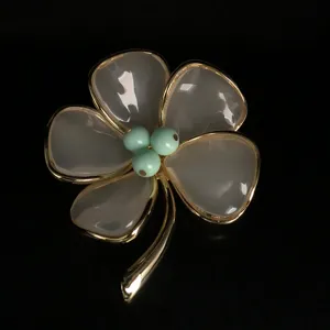 Close-up detail of a vintage style four-petal flower brooch with gold edges and translucent design.