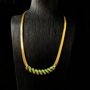 Detailopname van de retro gouden ketting met groene emaillering en schitterende strass-steentjes.