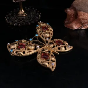 Detailopname van de vintage gouden vlinderbroche ingelegd met rode stenen en parels.