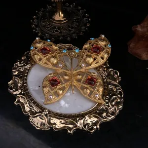 Detail van gouden vintage vlinderbroche met verfijnd filigraanwerk en opvallende rode kristalstenen.