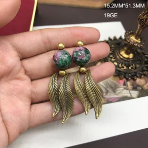 Detail view of retro distressed gold earrings featuring green stone beads and metal leaf pendants.