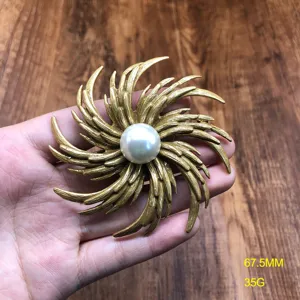 Vintage gold tone textured sunburst brooch featuring a central white pearl. Detail shot.