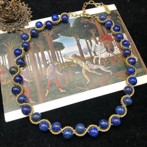Detailed vintage-style gold-tone woven necklace featuring rich blue stone beads and clasp.
