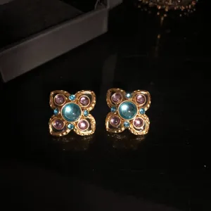 Detailed shot of retro gold-tone floral earrings featuring blue glass and purple stones.