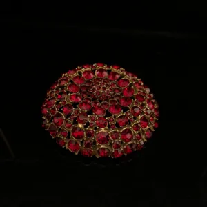 Primo piano di una spilla vintage a cupola con strass rossi e dettagli in metallo dorato.