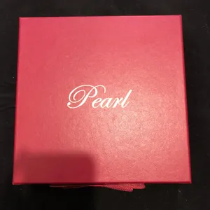 Détail de boîte à bijoux en cuir PU rouge avec surface texturée et écriture Pearl élégante.