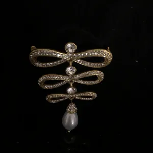 Close-up detail of vintage ornate gold-toned rhinestone bow brooch with pearl drop.