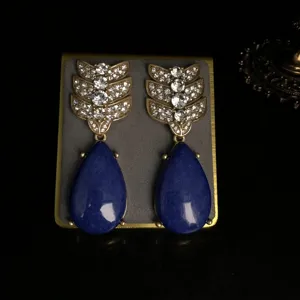 Detalle en primer plano de pendientes retro dorados con hojas de pedrería fina.