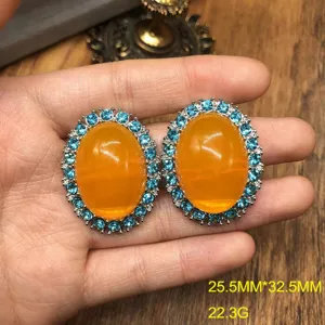 Close-up detail shot of vintage oval orange stone earrings featuring blue crystal halo trim.