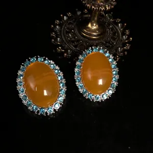 Close-up detail of vintage retro oval orange stone earrings with blue rhinestone border.