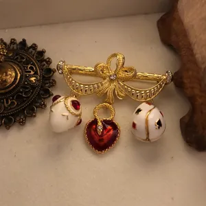 Spilla vintage color oro con fiocco, cuore in smalto e ciondoli uovo di carte.