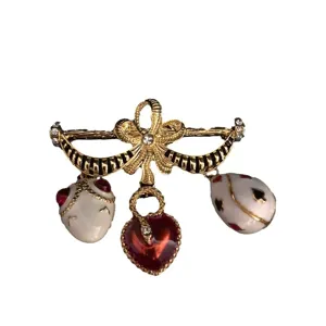 Spilla vintage con fiocco smaltato e ciondoli pendenti a cuore e uovo, elegante gioiello dorato.