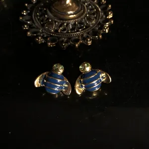 Close-up detail of luxury blue enamel gold bee stud earrings featuring sparkling green crystal eyes.