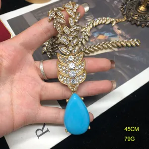 Detalle de primer plano de collar hoja de estrás oro vintage con gota de turquesa.