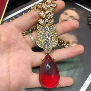 Detalle del collar vintage dorado con hojas de cristal y un colgante de piedra roja.