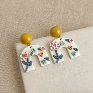 Nahaufnahme von handgefertigten Polymer-Ton Blumen Bogen Ohrringen mit gelbem Kugelstecker.