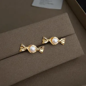 Nahaufnahme von goldenen Perlen-Ohrringen in Bonbon-Form auf braunem Samt, elegantes Schmuckstück