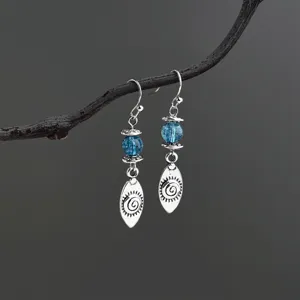Close-up detail of vintage silver-tone drop earrings with blue beads and spiral sun pendants.