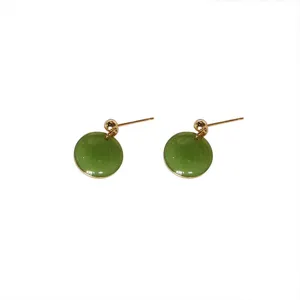Close-up detail of green round stud earrings with gold metal trim, elegant minimalist jewelry.