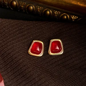 Close-up of French vintage geometric earrings with red stone and gold frame on dark knit.